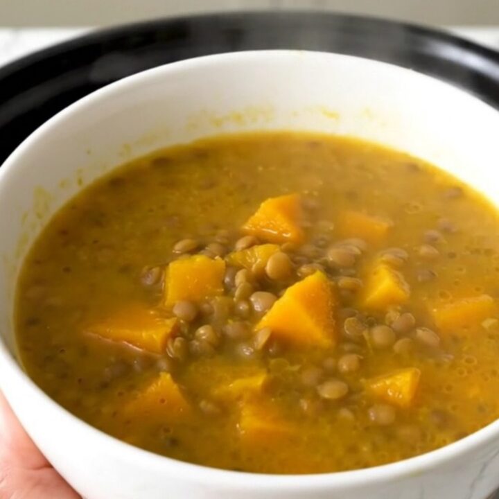 A rustic bowl of lentil and pumpkin soup steaming in a bright kitchen setting.