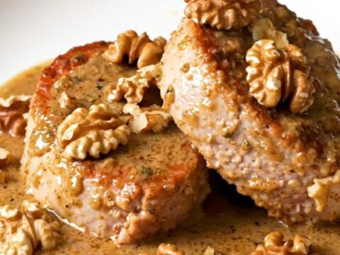 A close-up of thick, juicy pork tenderloin medallions covered in a creamy, rich Roquefort sauce with scattered walnut pieces.