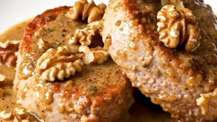 A close-up of thick, juicy pork tenderloin medallions covered in a creamy, rich Roquefort sauce with scattered walnut pieces.