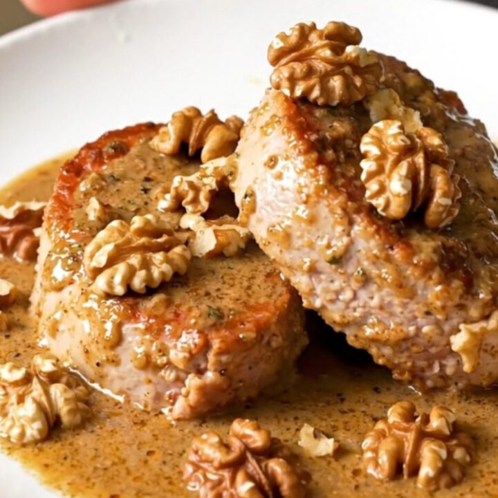 A close-up of thick, juicy pork tenderloin medallions covered in a creamy, rich Roquefort sauce with scattered walnut pieces.