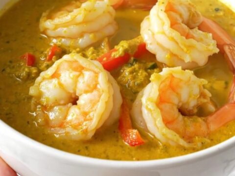 A top-down view of a creamy coconut lime shrimp curry in a black slow cooker on a quartz countertop.