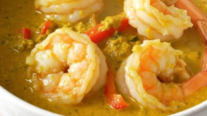 A top-down view of a creamy coconut lime shrimp curry in a black slow cooker on a quartz countertop.