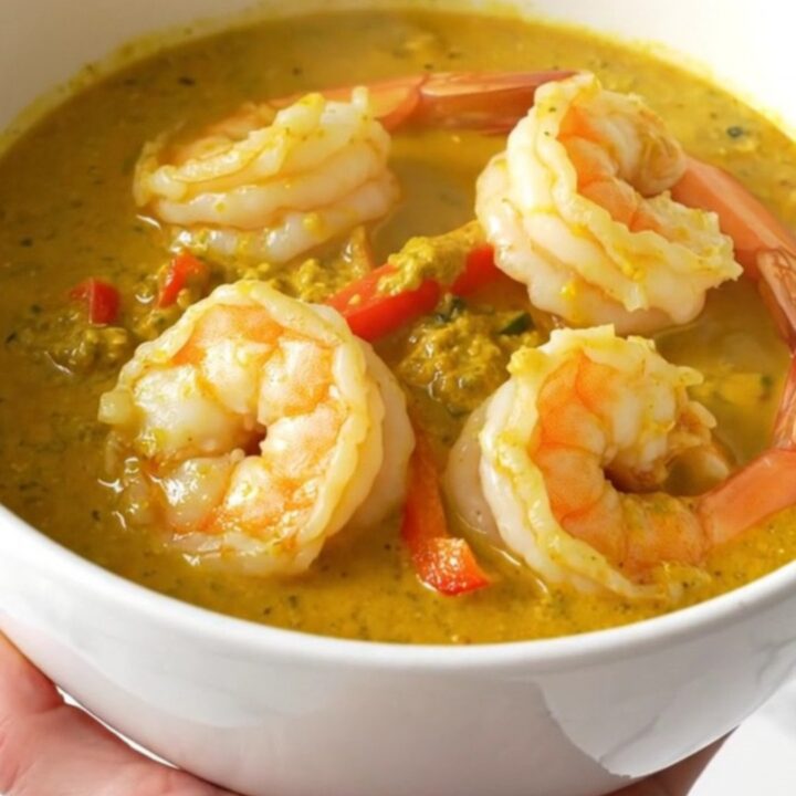 A top-down view of a creamy coconut lime shrimp curry in a black slow cooker on a quartz countertop.