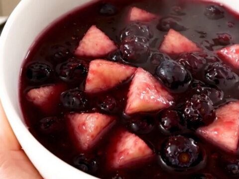 A close-up of a glossy, purple apple and wild blueberry compote in a white ceramic bowl.