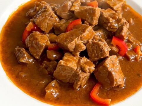 A steaming plate of Basque pork axoa with tender pork and colorful peppers.