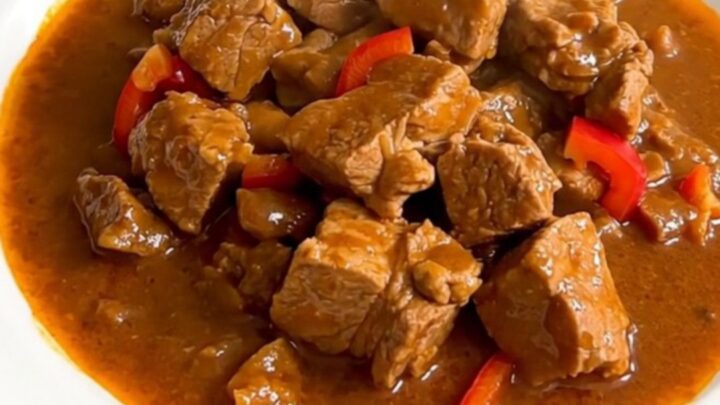 A steaming plate of Basque pork axoa with tender pork and colorful peppers.