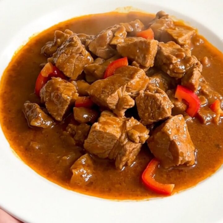 A steaming plate of Basque pork axoa with tender pork and colorful peppers.