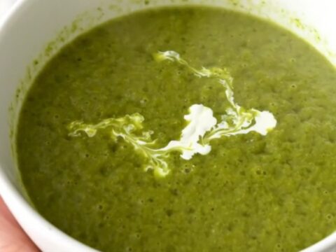 A vibrant green pea and leek velouté in a white bowl with a cream swirl.