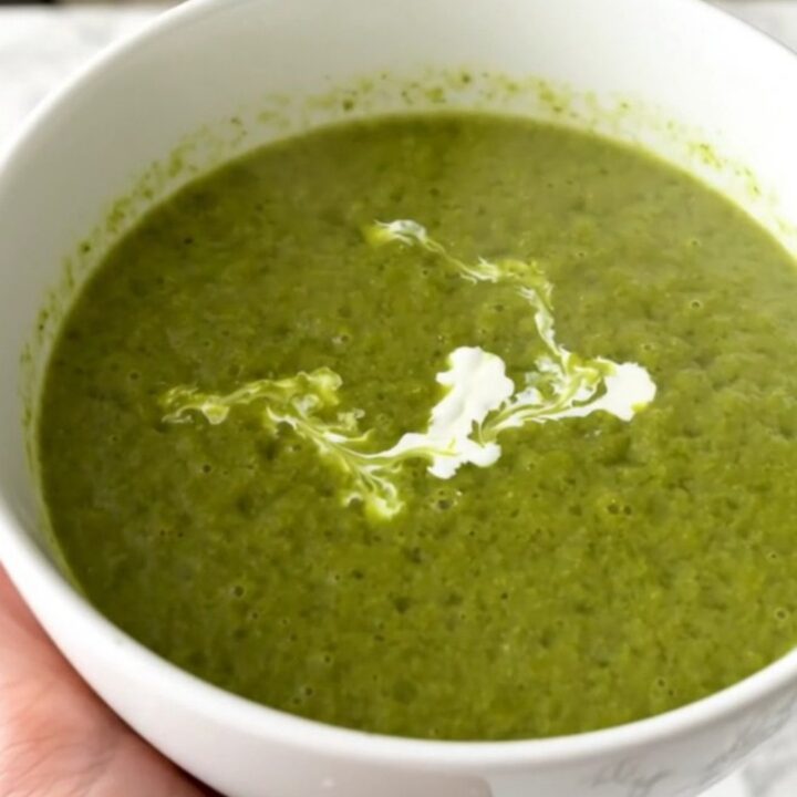A vibrant green pea and leek velouté in a white bowl with a cream swirl.