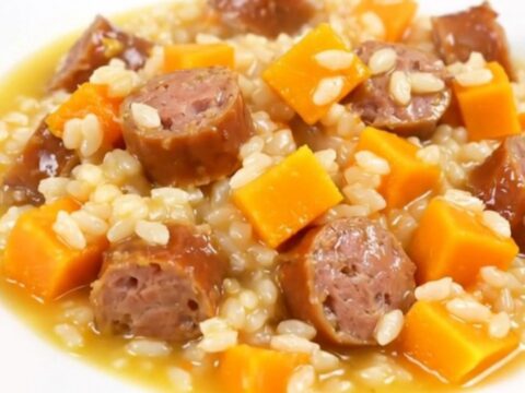 A top-down view of a black slow cooker insert filled with raw sausage, butternut squash