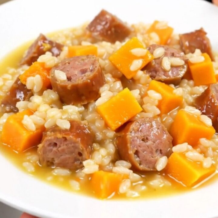 A top-down view of a black slow cooker insert filled with raw sausage, butternut squash