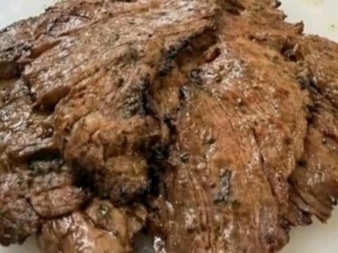 A stacked pile of seared, juicy marinated flank steak slices resting on a white cutting board.