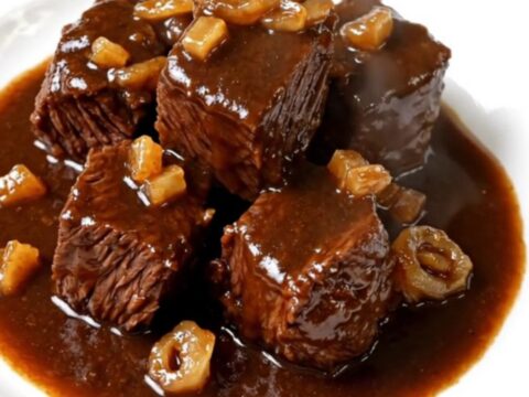 A close-up of a steaming bowl of beef bourguignon with glossy sauce and tender shallots.