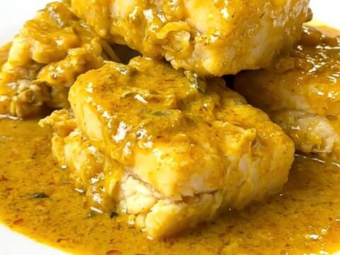 A steaming, glossy portion of coconut curry cod served on a white plate with visible zucchini and red bell pepper.