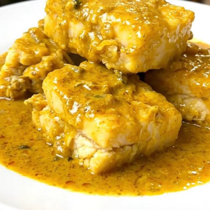 A steaming, glossy portion of coconut curry cod served on a white plate with visible zucchini and red bell pepper.