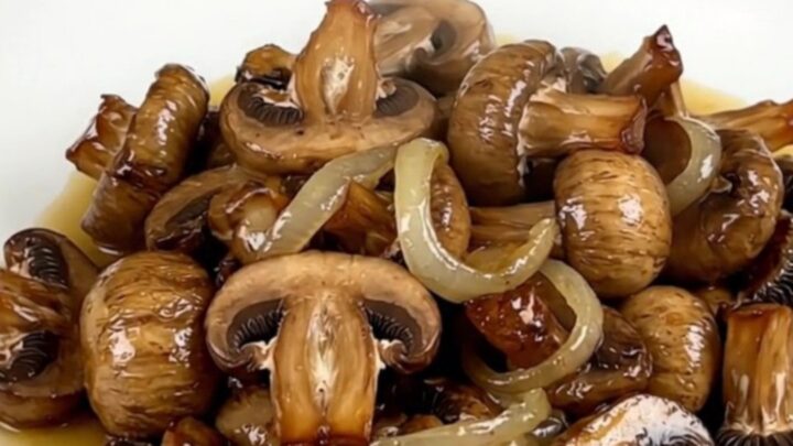A close-up of glossy, wine-braised mushrooms in a white bowl with fresh aromatics.