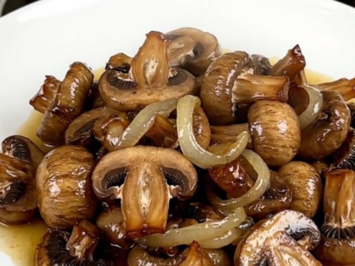 A close-up of glossy, wine-braised mushrooms in a white bowl with fresh aromatics.