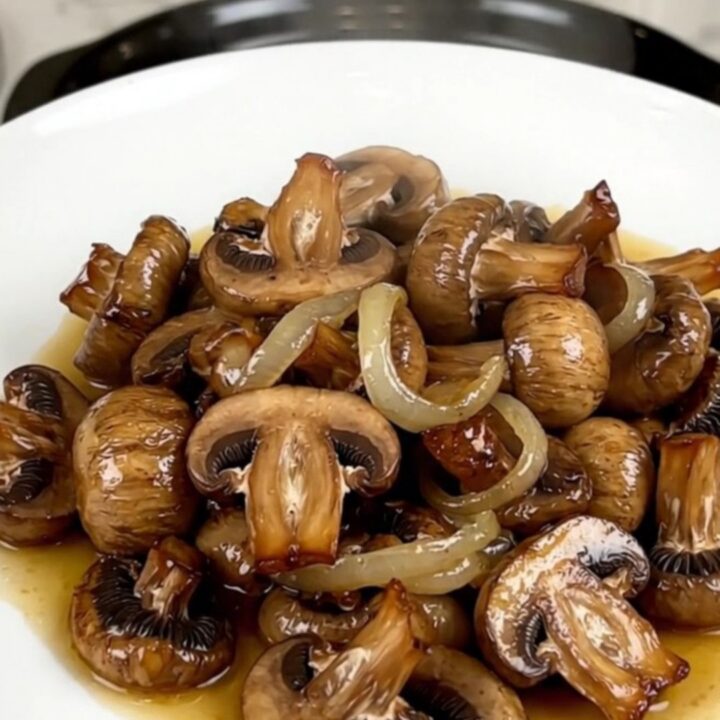 A close-up of glossy, wine-braised mushrooms in a white bowl with fresh aromatics.