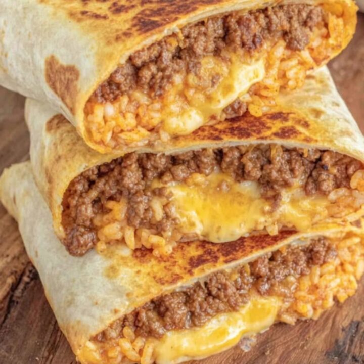 A stack of three halved crispy grilled burritos on a rustic wooden board, showing gooey cheese and seasoned beef.