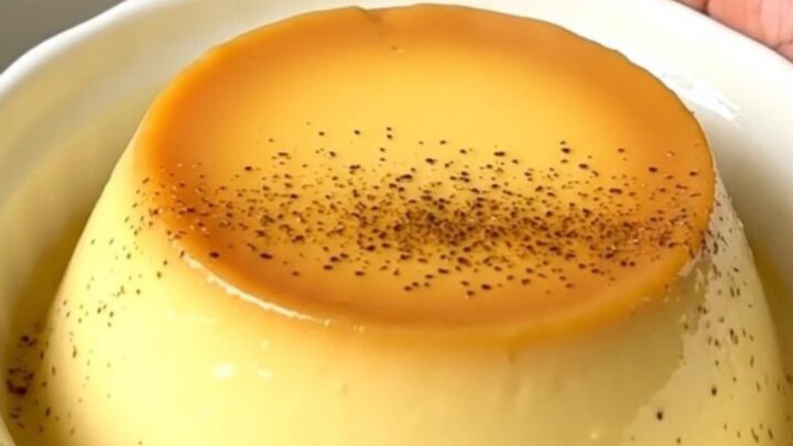 A close-up of creamy vanilla egg custard in a white ceramic dish, steaming slightly with a dusting of nutmeg.