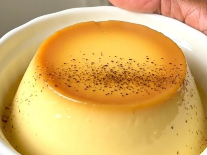 A close-up of creamy vanilla egg custard in a white ceramic dish, steaming slightly with a dusting of nutmeg.