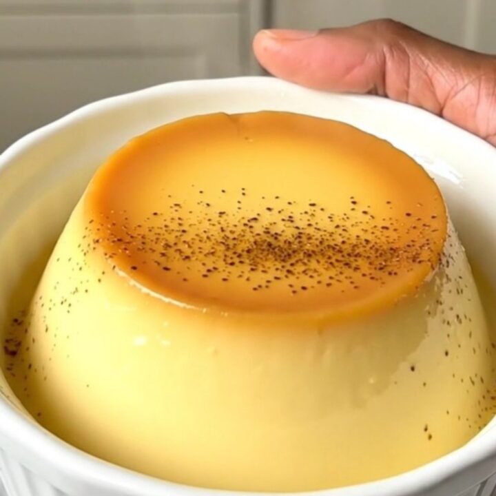 A close-up of creamy vanilla egg custard in a white ceramic dish, steaming slightly with a dusting of nutmeg.