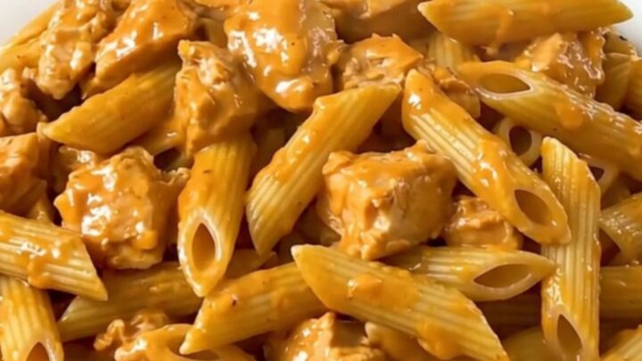 A top-down view of a slow cooker filled with chicken, penne, and tomato sauce before cooking.