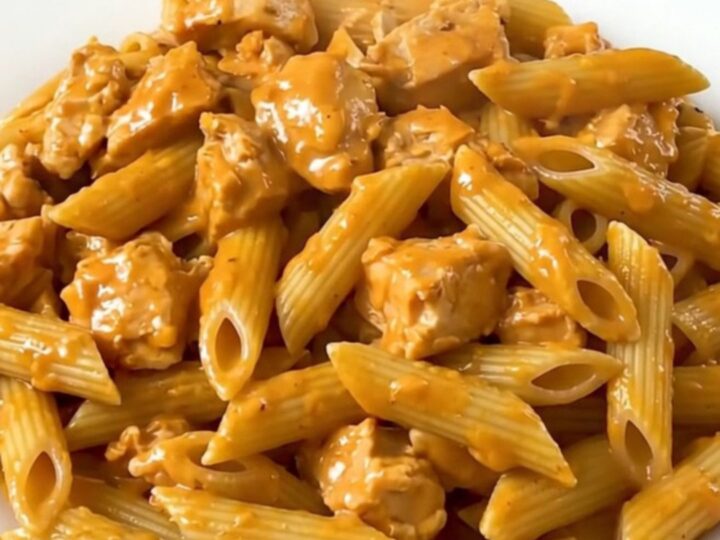 A top-down view of a slow cooker filled with chicken, penne, and tomato sauce before cooking.