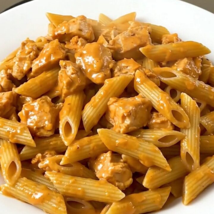 A top-down view of a slow cooker filled with chicken, penne, and tomato sauce before cooking.