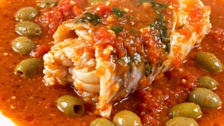 A close-up of monkfish stew in a slow cooker with visible tomatoes, capers, and green olives.