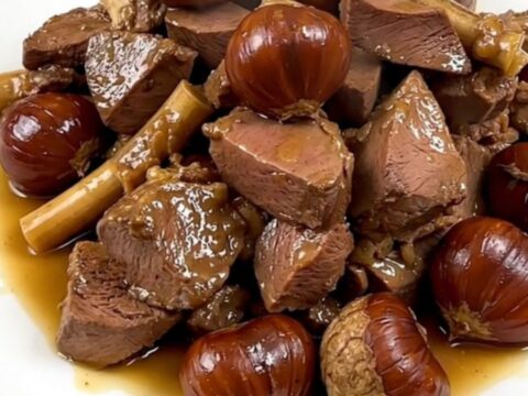 A close-up view of tender braised veal tendrons and whole chestnuts served on a white plate.
