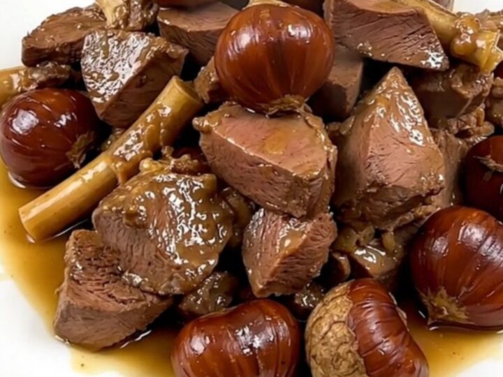 A close-up view of tender braised veal tendrons and whole chestnuts served on a white plate.