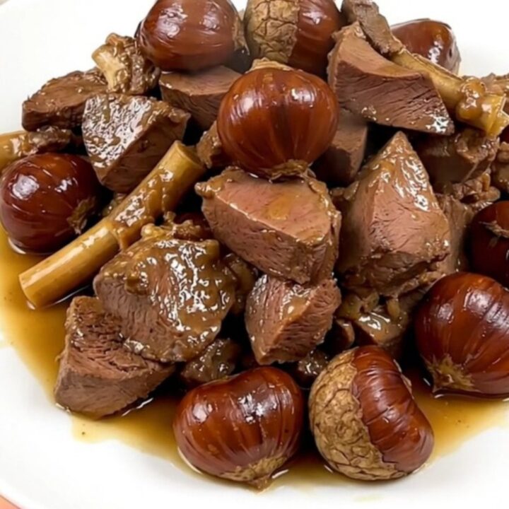 A close-up view of tender braised veal tendrons and whole chestnuts served on a white plate.