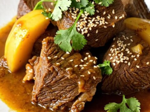 A close-up of a slow cooker beef tagine with quince and cinnamon served on a white plate.
