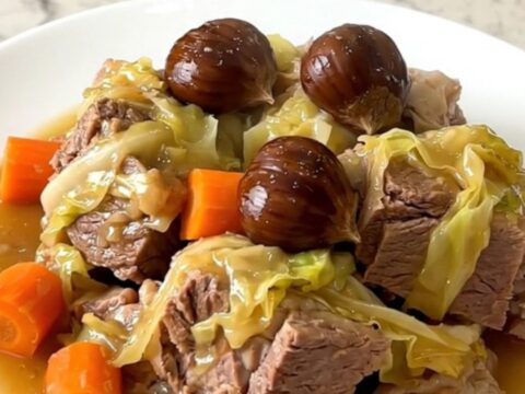 A rustic slow cooker potée with salt pork, sausages, cabbage, and chestnuts in a white bowl.
