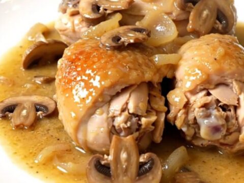 A top-down view of chicken pieces, mushrooms, and shallots cooking in a black slow cooker on a white countertop.