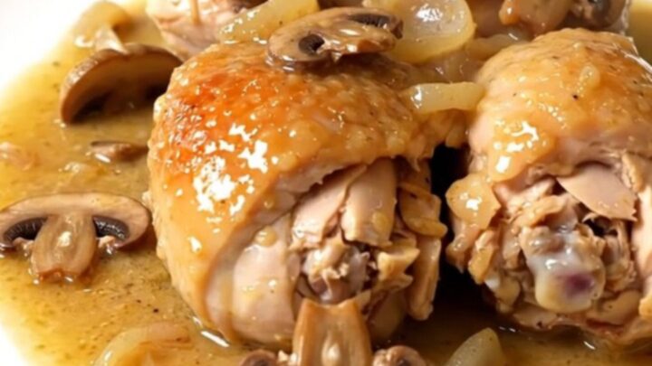 A top-down view of chicken pieces, mushrooms, and shallots cooking in a black slow cooker on a white countertop.