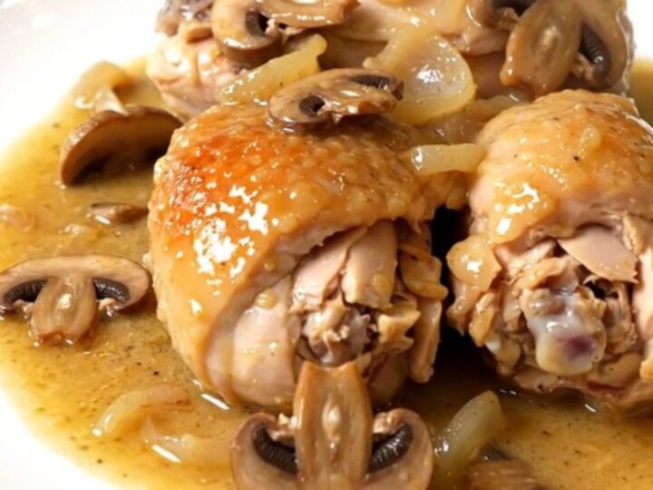 A top-down view of chicken pieces, mushrooms, and shallots cooking in a black slow cooker on a white countertop.