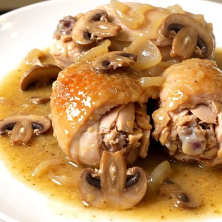 A top-down view of chicken pieces, mushrooms, and shallots cooking in a black slow cooker on a white countertop.