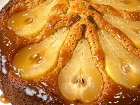 A golden, caramelized pear upside-down cake served on a plain white round plate, with a glossy finish.
