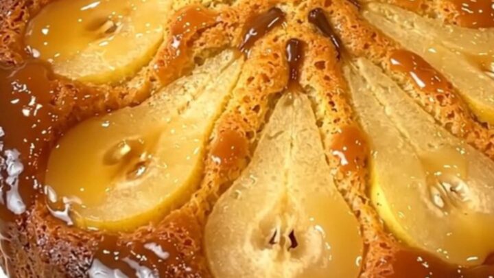 A golden, caramelized pear upside-down cake served on a plain white round plate, with a glossy finish.