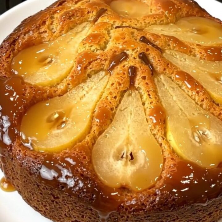 A golden, caramelized pear upside-down cake served on a plain white round plate, with a glossy finish.