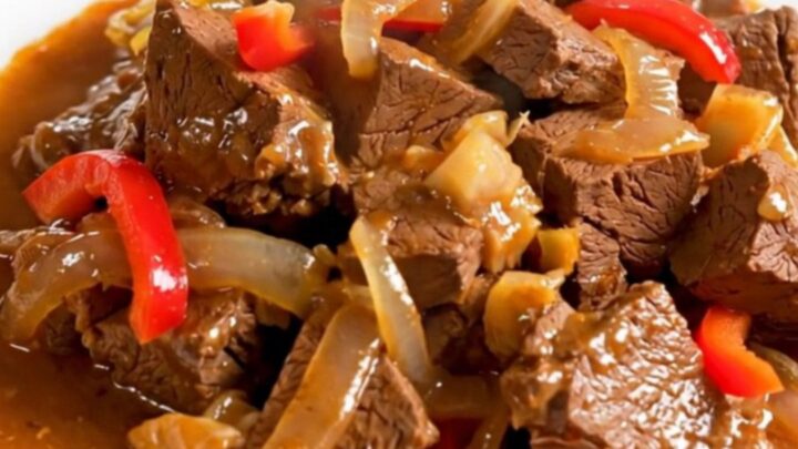 A top-down view of a slow cooker filled with raw veal, colorful peppers, and onions ready to be cooked.