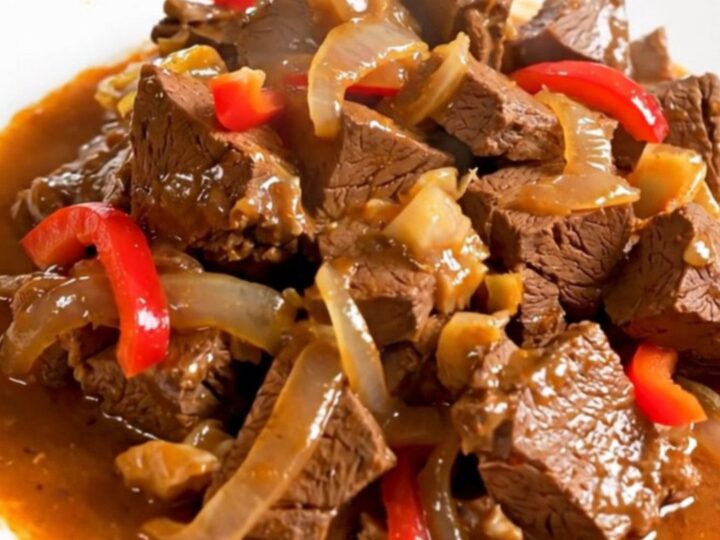 A top-down view of a slow cooker filled with raw veal, colorful peppers, and onions ready to be cooked.