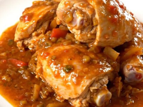 A white plate filled with slow cooker massale chicken, potatoes, and onions in a rich tomato sauce.