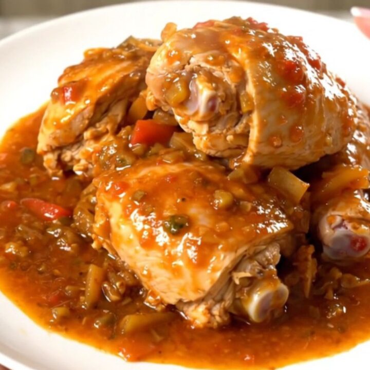 A white plate filled with slow cooker massale chicken, potatoes, and onions in a rich tomato sauce.
