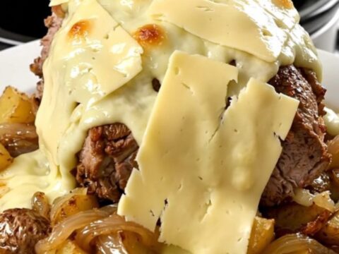 A rustic slow cooker pork roast topped with melted Reblochon cheese and potatoes in a black slow cooker.