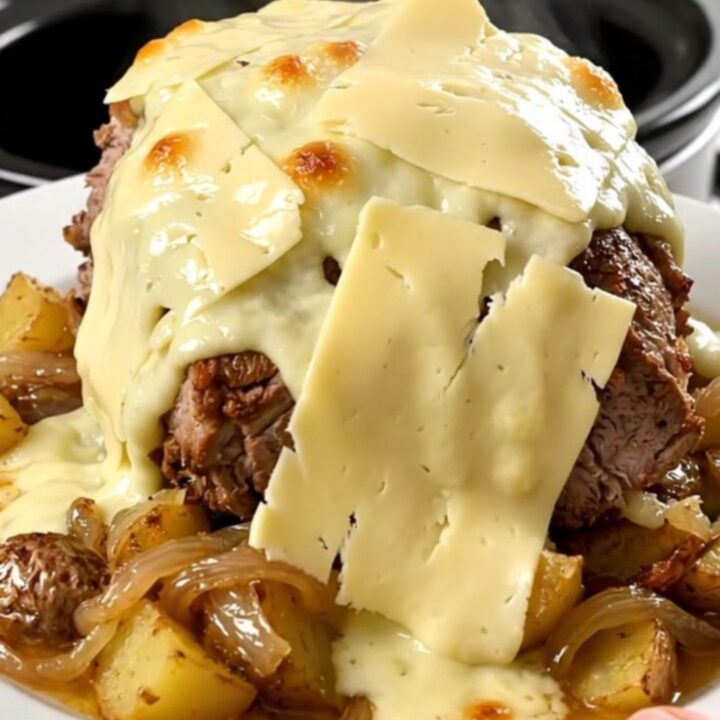A rustic slow cooker pork roast topped with melted Reblochon cheese and potatoes in a black slow cooker.