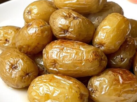 A close-up of tender, steaming boulangere potatoes served on a plain white plate with a soft-focus kitchen background.