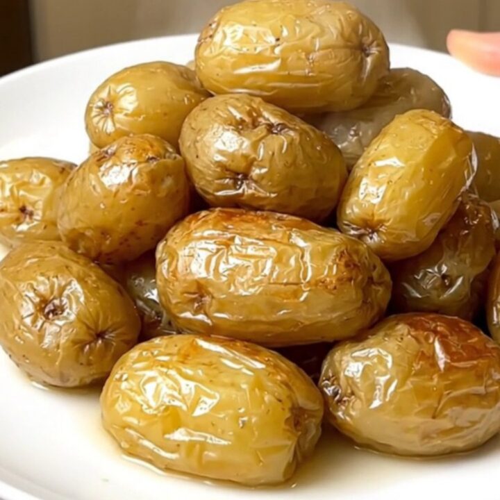A close-up of tender, steaming boulangere potatoes served on a plain white plate with a soft-focus kitchen background.